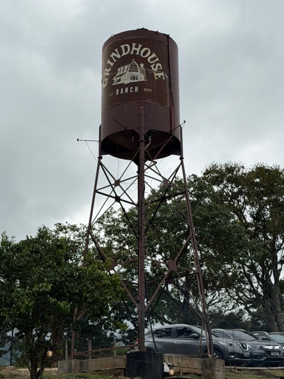 Caixa d'água com o logo Grindhouse Ranch EST 2024 vista ampla com estacionamento da fazenda