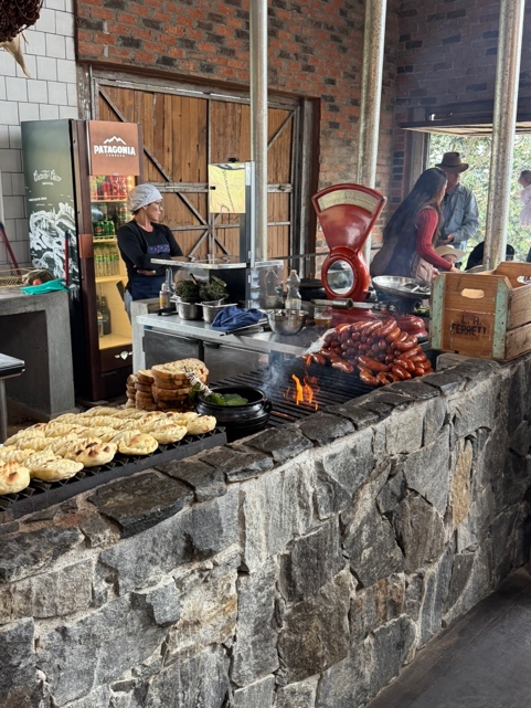 Parrilla aberta do Grindhouse Ranch com chef cortando linguiças, balança vintage vermelha, empanadas prontas e fumaça