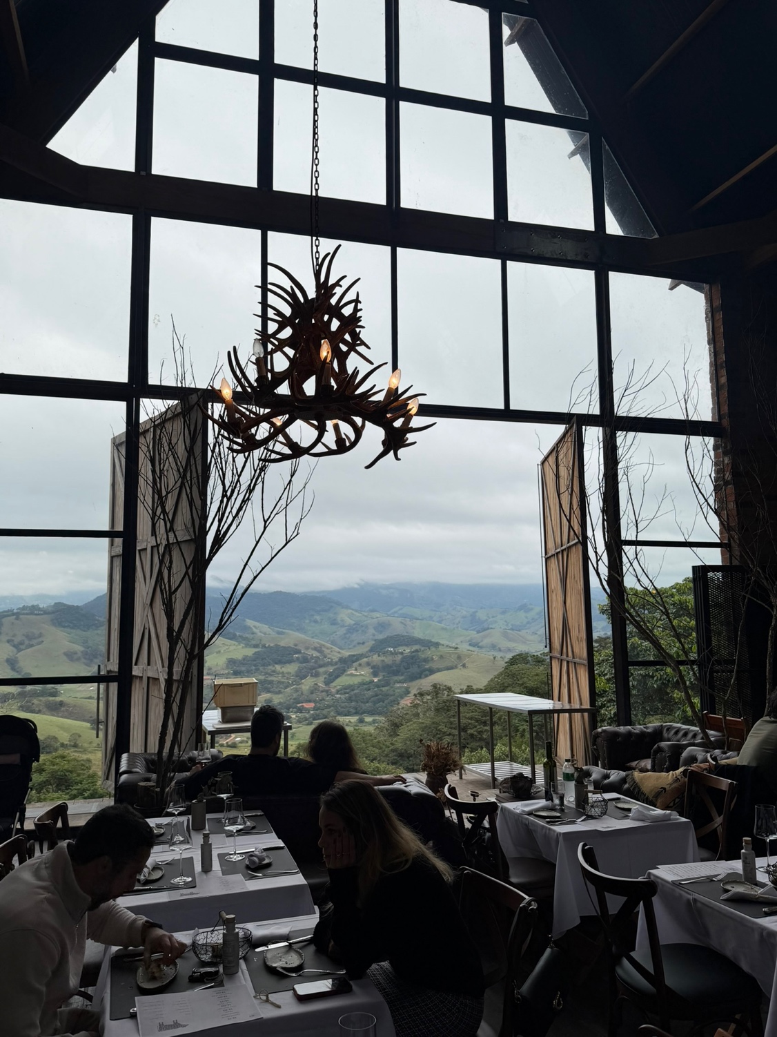 Interior do salão Grindhouse Ranch com pé direito de doze metros, lustre de chifre de cervo e vista panorâmica da Serra da Mantiqueira