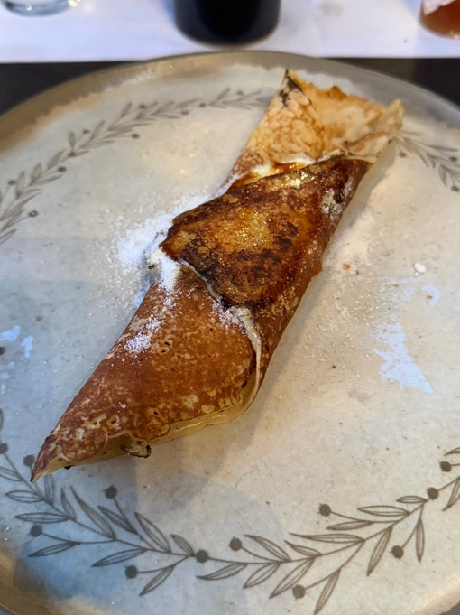 Panqueca argentina dobrada de doce de leite com açúcar de confeiteiro em prato de cerâmica artesanal com detalhes de folhagem