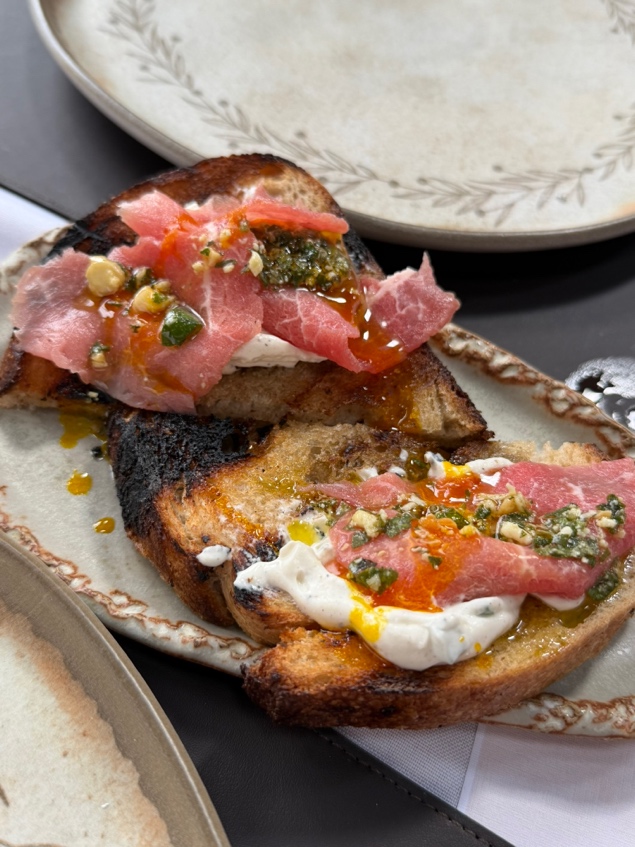 Brusqueta de pão sourdough tostado com sour cream, azeite de dendê e carne crua finíssima por cima, servida no domingo do Grindhouse Ranch