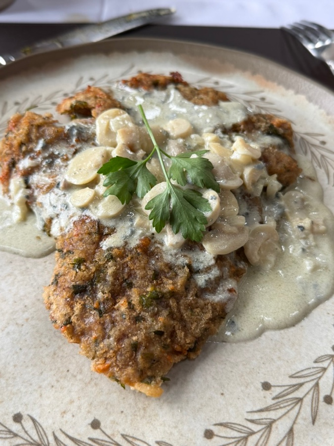 Milanesa empanada com molho de gorgonzola, cogumelos fatiados e salsinha por cima, em prato de cerâmica artesanal