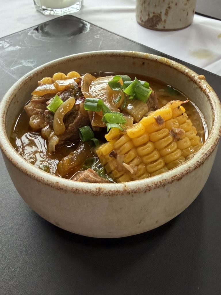 Locro argentino servido em tigela rústica, com pedaços de milho na espiga, carne, cebola e cebolinha picada