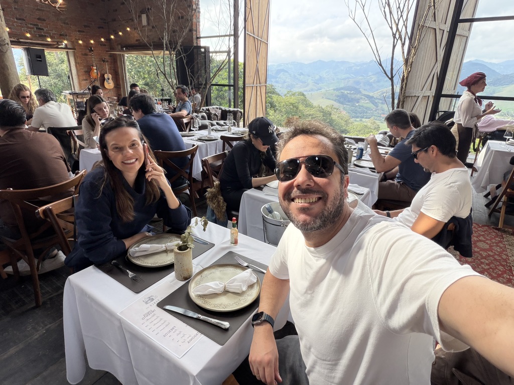 Casal a mesa no salão Grindhouse Ranch, com mesa posta, vinho e a vista das montanhas da Serra da Mantiqueira ao fundo