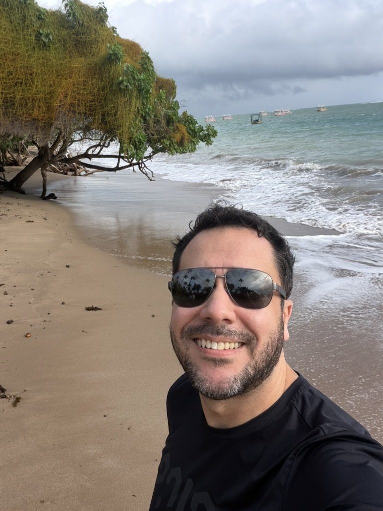 Pé na areia da Praia do Patacho, com árvore inclinada sobre a faixa de areia e o mar verde